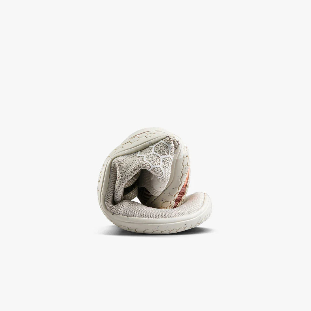Light gray flexible running shoe rolled up on white background showing sole with hexagonal patterns