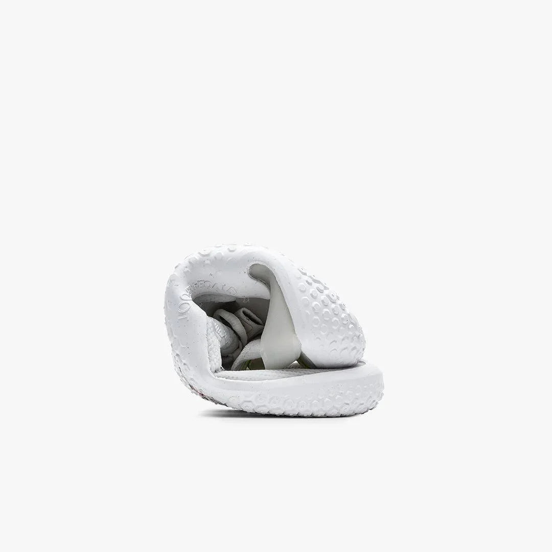 White flexible sneaker with textured sole curled into a compact folded shape on white background