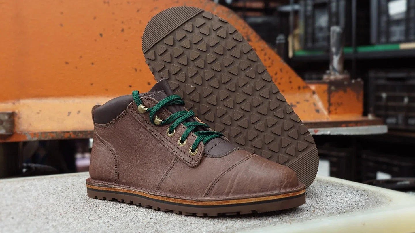 Brown sustainable barefoot shoe with green laces, eco-friendly design, on textured surface