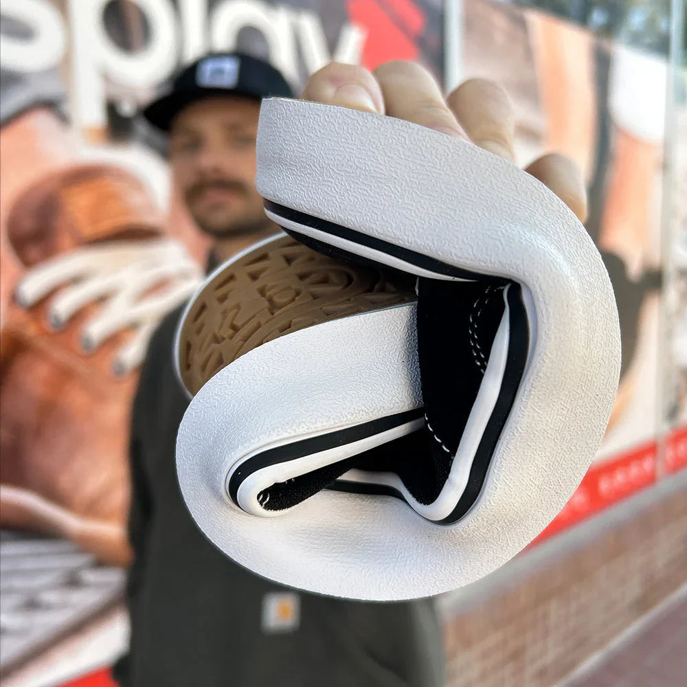 Flexible white and black sneaker sole bent to show its softness with blurred graffiti background