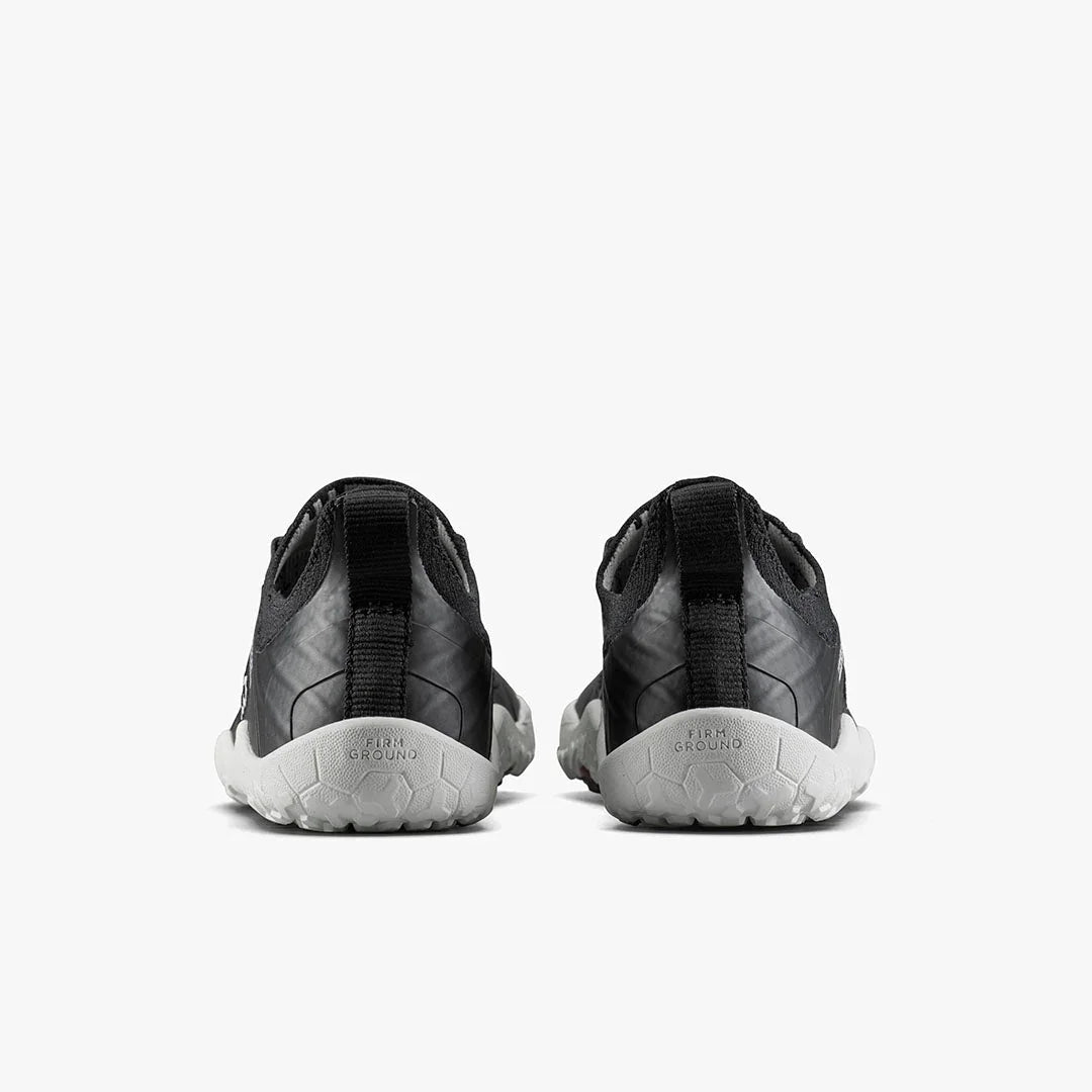 Pair of black minimalist athletic shoes with white textured firm ground soles viewed from the back