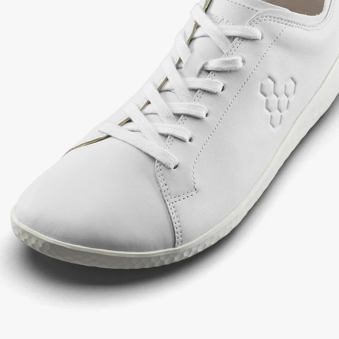 Close-up of white leather sneaker with honeycomb pattern logo and white laces on white background