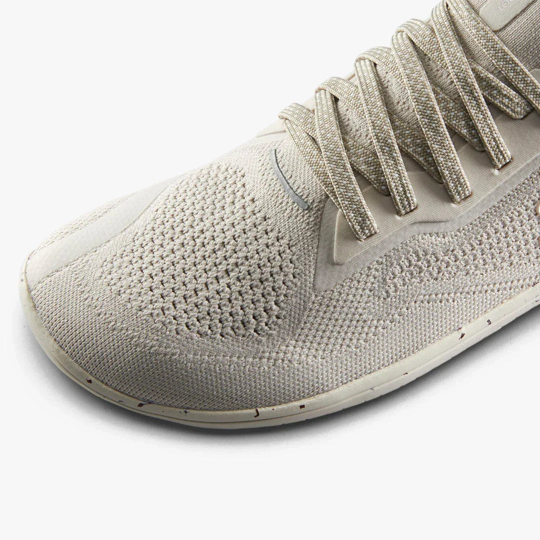 Close-up of beige knitted sneaker toe with textured fabric and light brown laces on white background