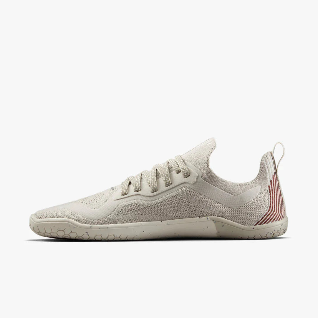 Beige minimalist knit sneaker with textured sole and red striped heel tab on white background