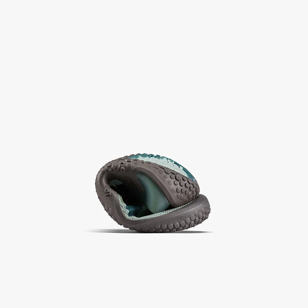 Folded flexible outdoor shoe with textured rubber sole and teal mesh upper on white background