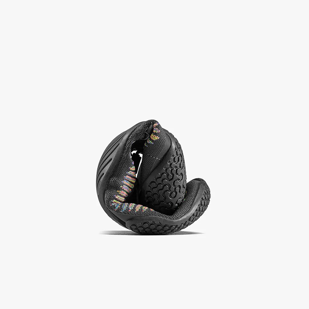 Black flexible barefoot shoe curled up showing textured sole and multicolor knit interior