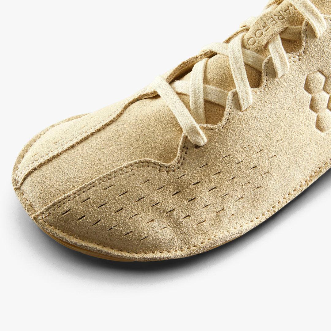 Close-up of beige suede barefoot shoe toe with detailed stitching and laces on white background