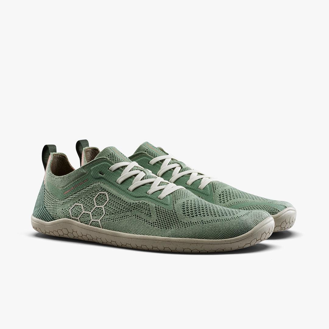 Pair of green minimalist running shoes with white laces and honeycomb-patterned sole on white background