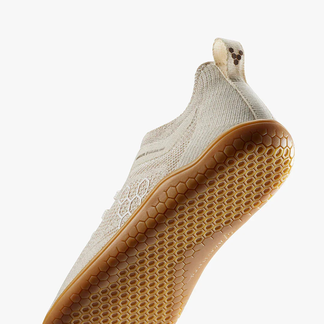 Close-up of beige knit sneaker with honeycomb-patterned gum sole and pull tab detail