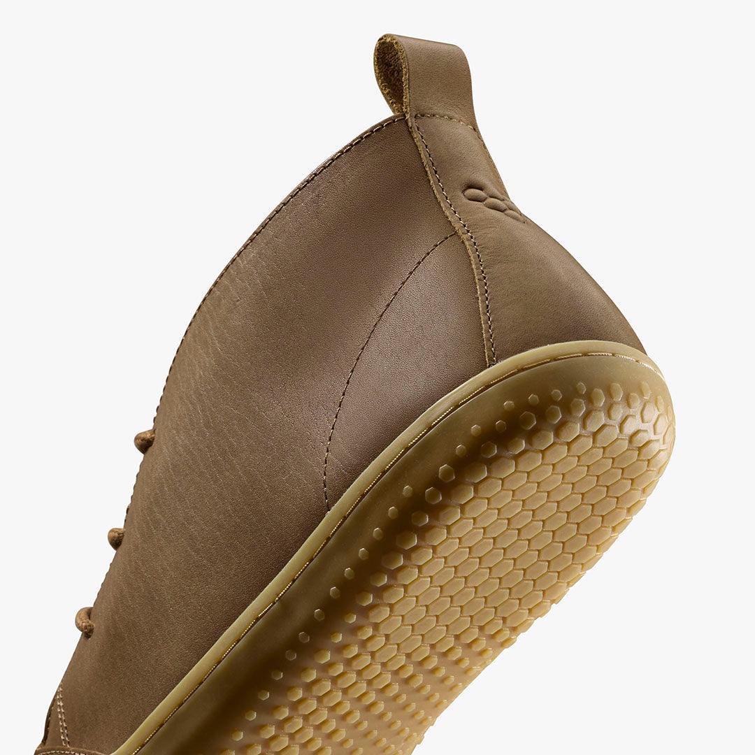 Close-up of brown leather shoe with textured honeycomb rubber sole and pull tab on white background