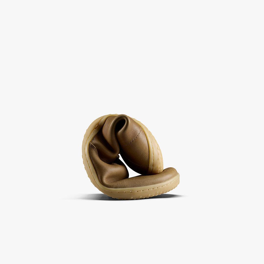 Flexible brown leather shoe with beige sole rolled up against white background