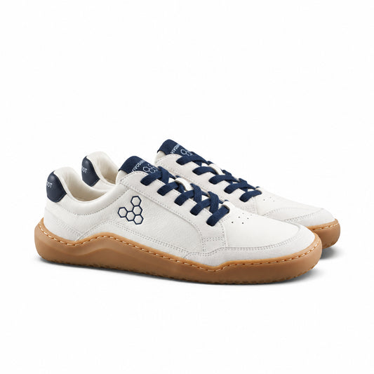 A pair of low-top sneakers in off-white leather with navy blue laces, navy blue heel tab, and a tan gum sole, shown on a light gray background.