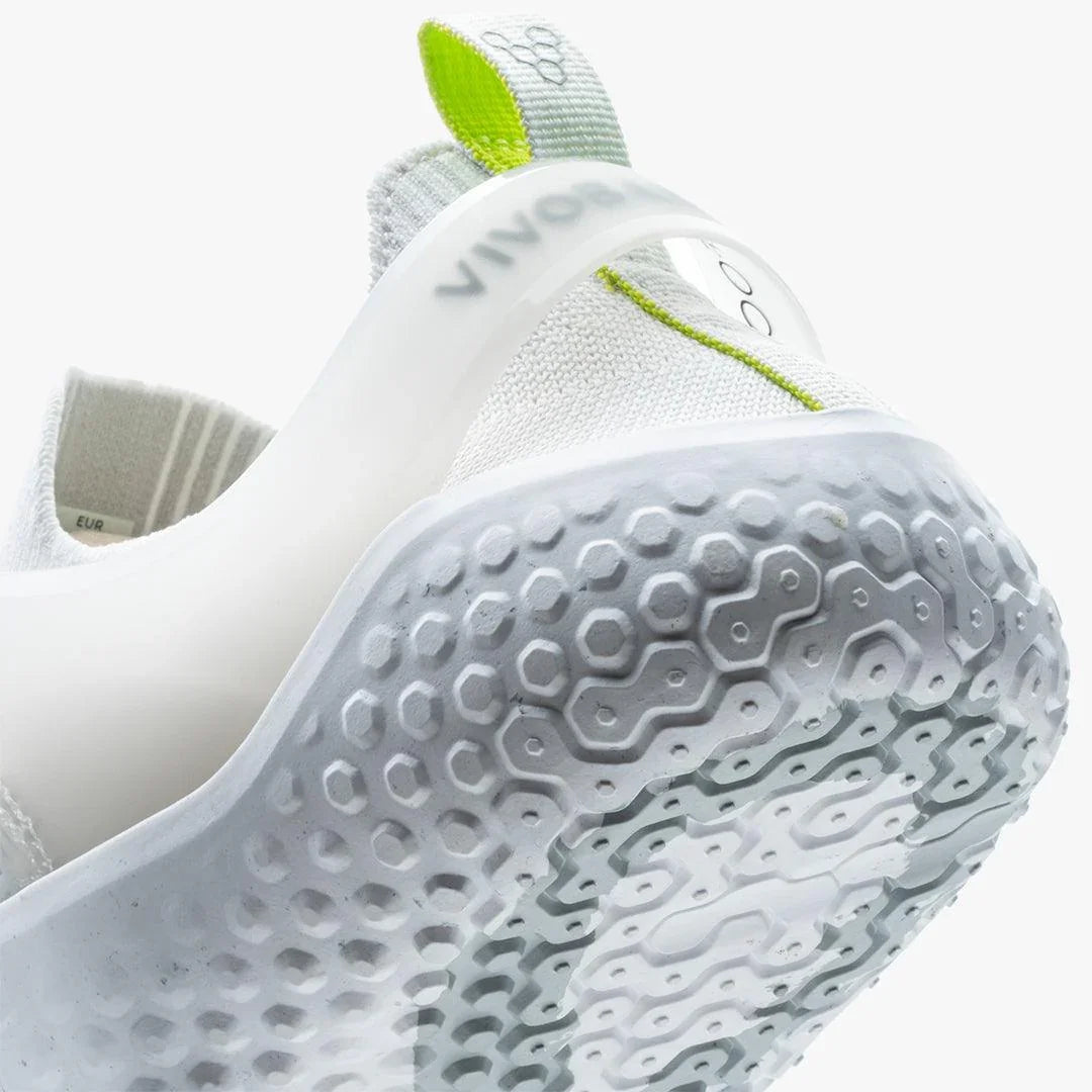 Closeup of white sneaker outsole with hexagonal tread and green stitch detail on knit fabric upper