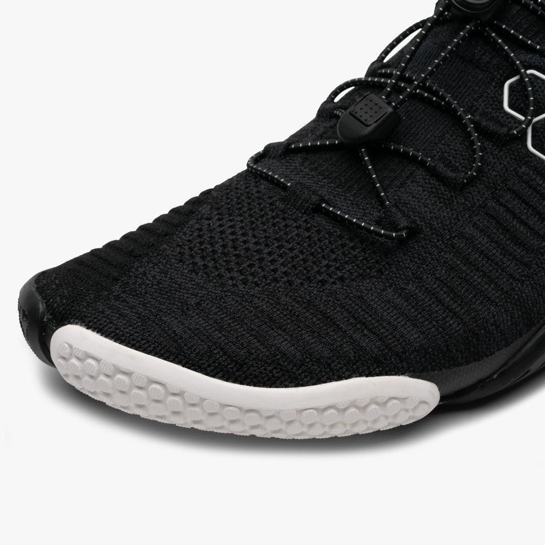 Close-up of black knit athletic shoe toe with white textured outsole and elastic laces