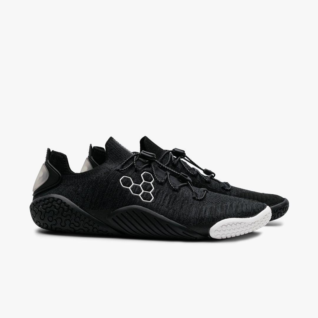 Pair of black minimalist athletic shoes with white hexagonal logo and textured sole on white background