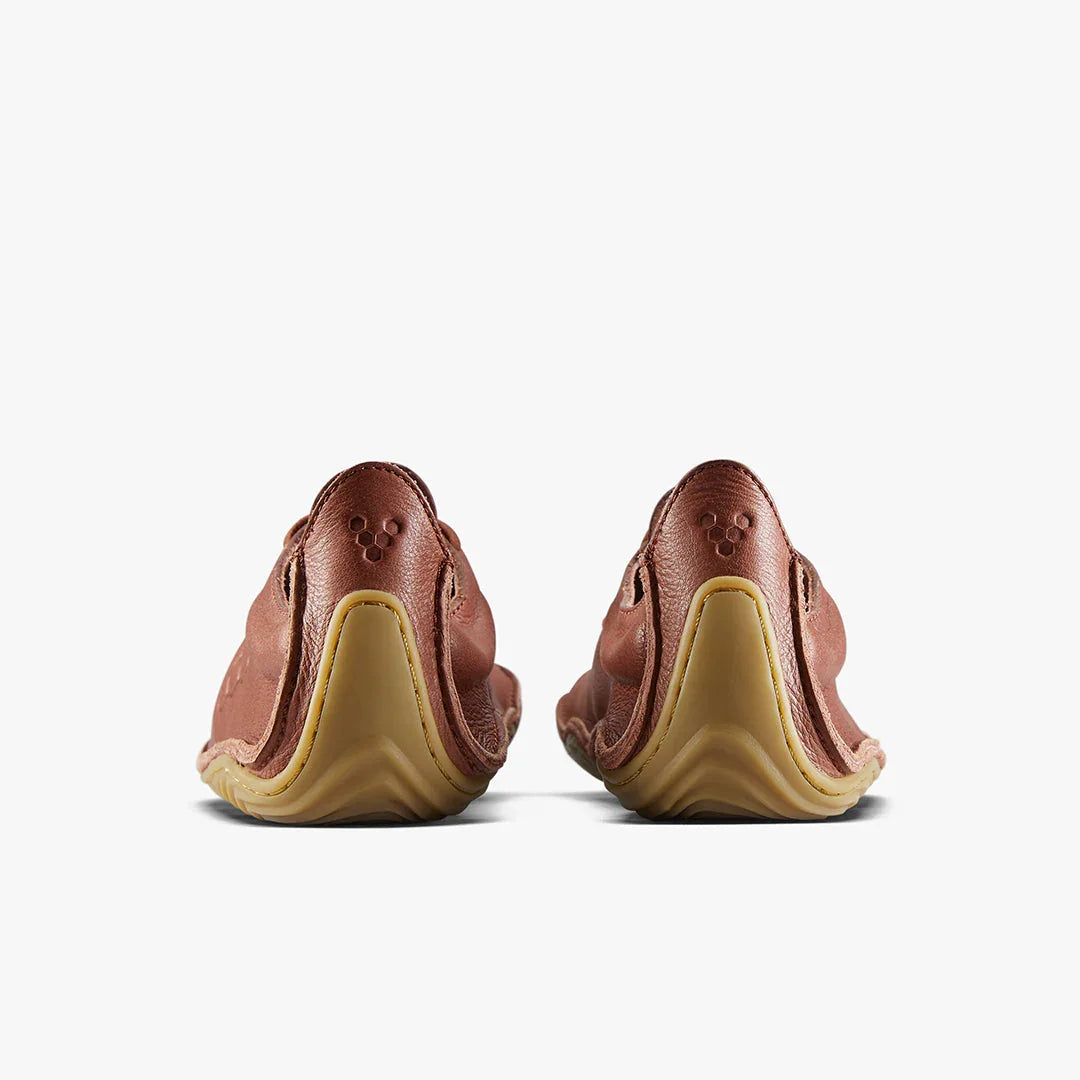 Rear view of brown leather minimalist shoes with textured rubber soles on white background