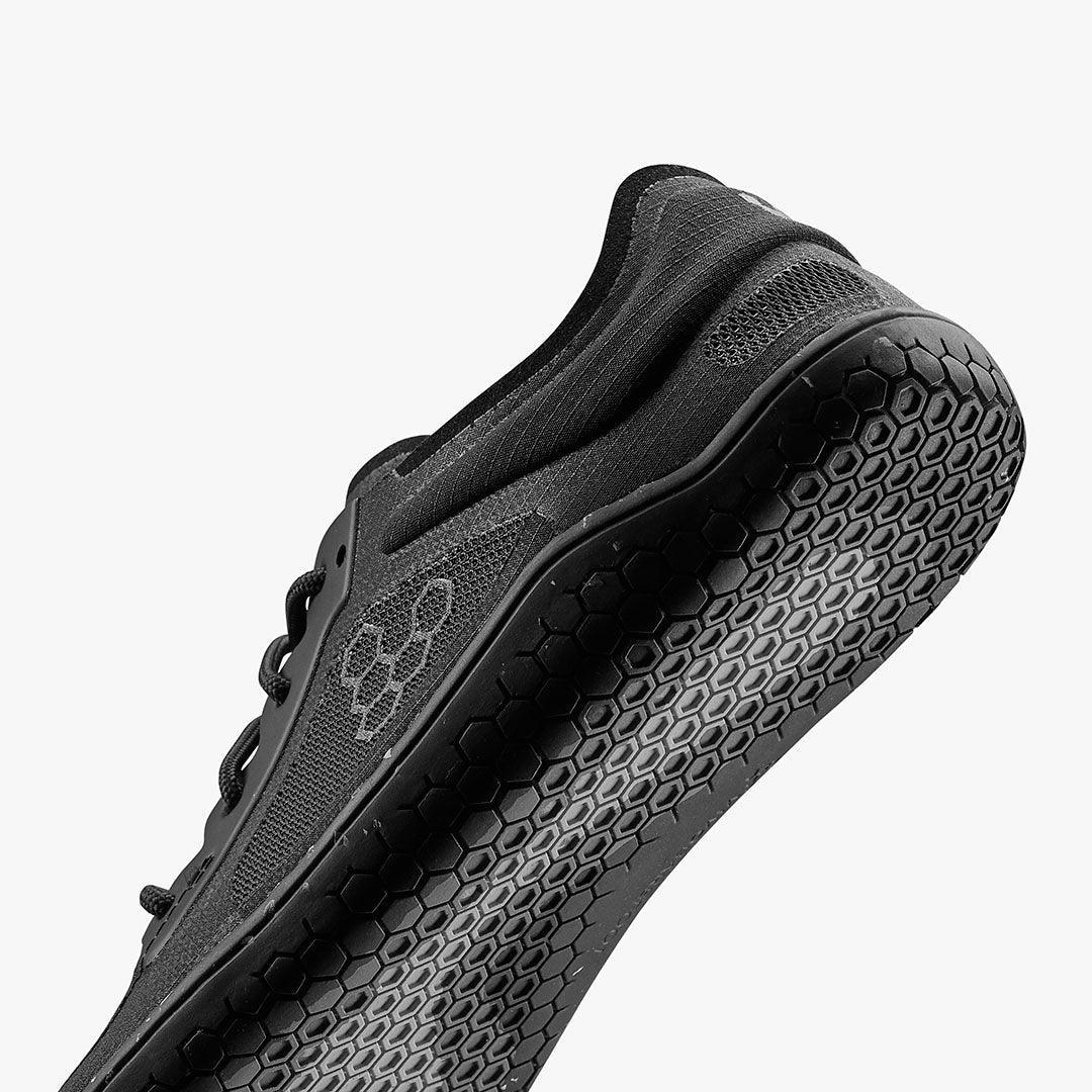 Closeup of black athletic shoe sole with hexagonal tread pattern and mesh upper