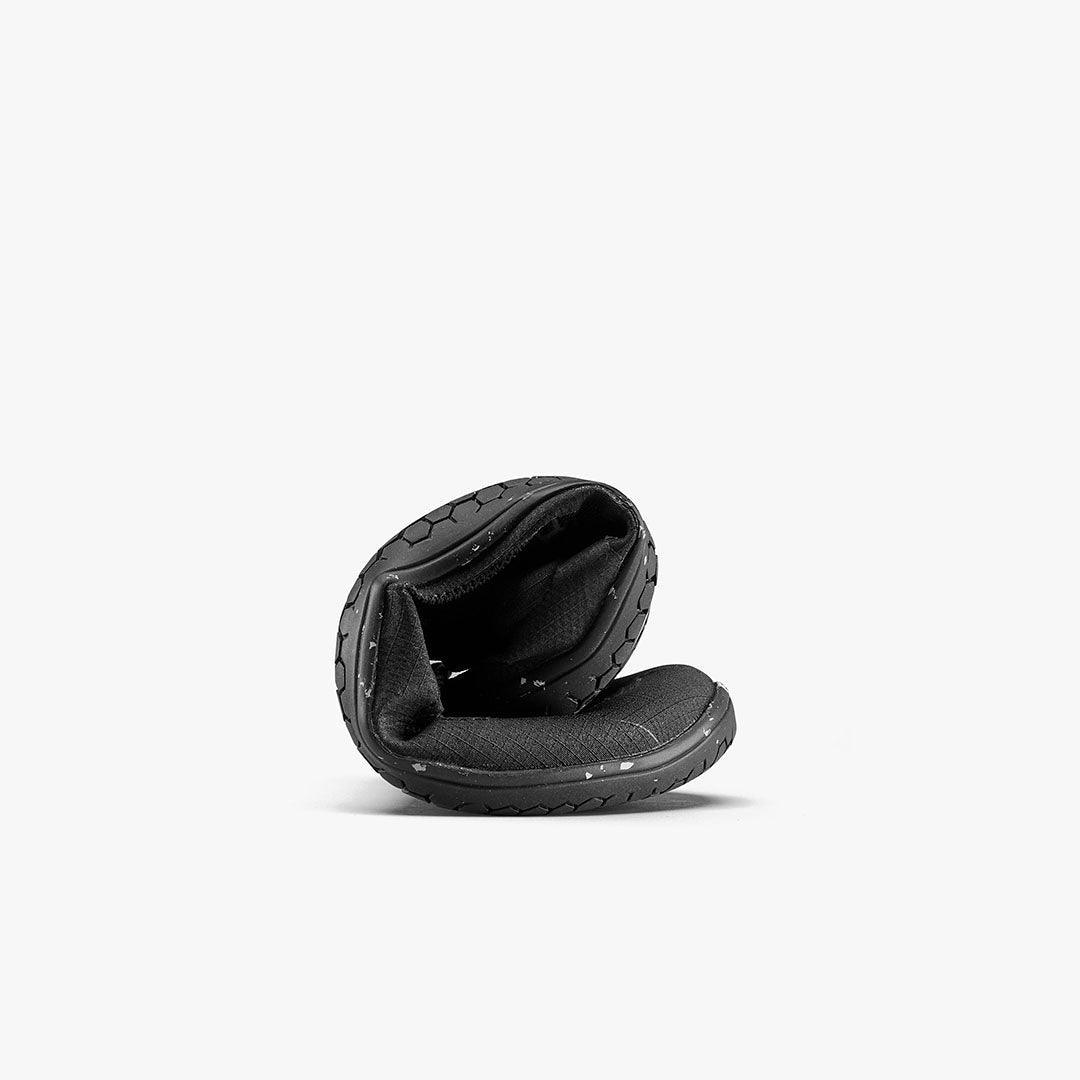 Black barefoot shoe curled to show flexible sole, sustainable footwear at The Grounded Sole