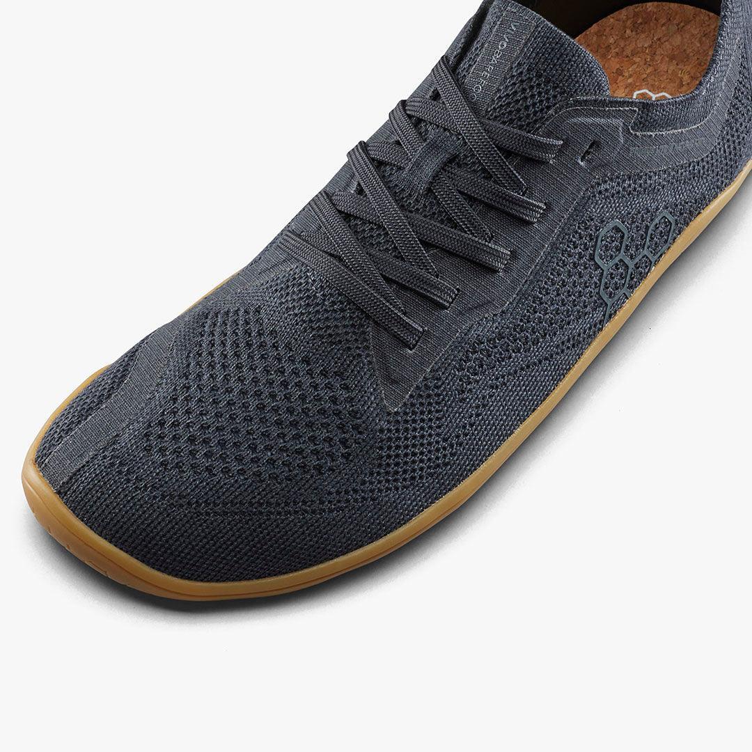 Close-up of black knitted lace-up sneaker with honeycomb pattern and gum sole on white background