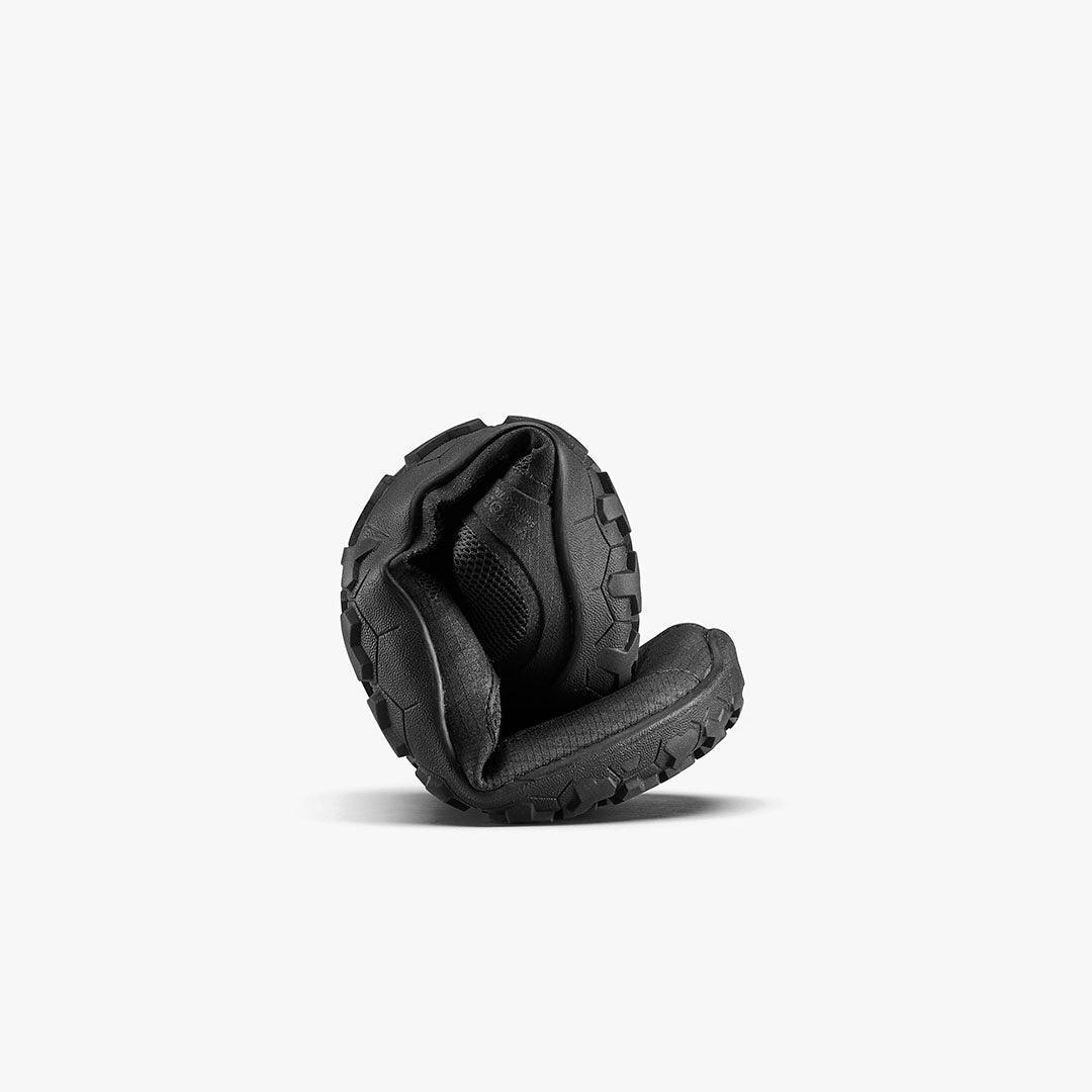 Flexible black barefoot shoe with rugged sole, curled to show natural movement