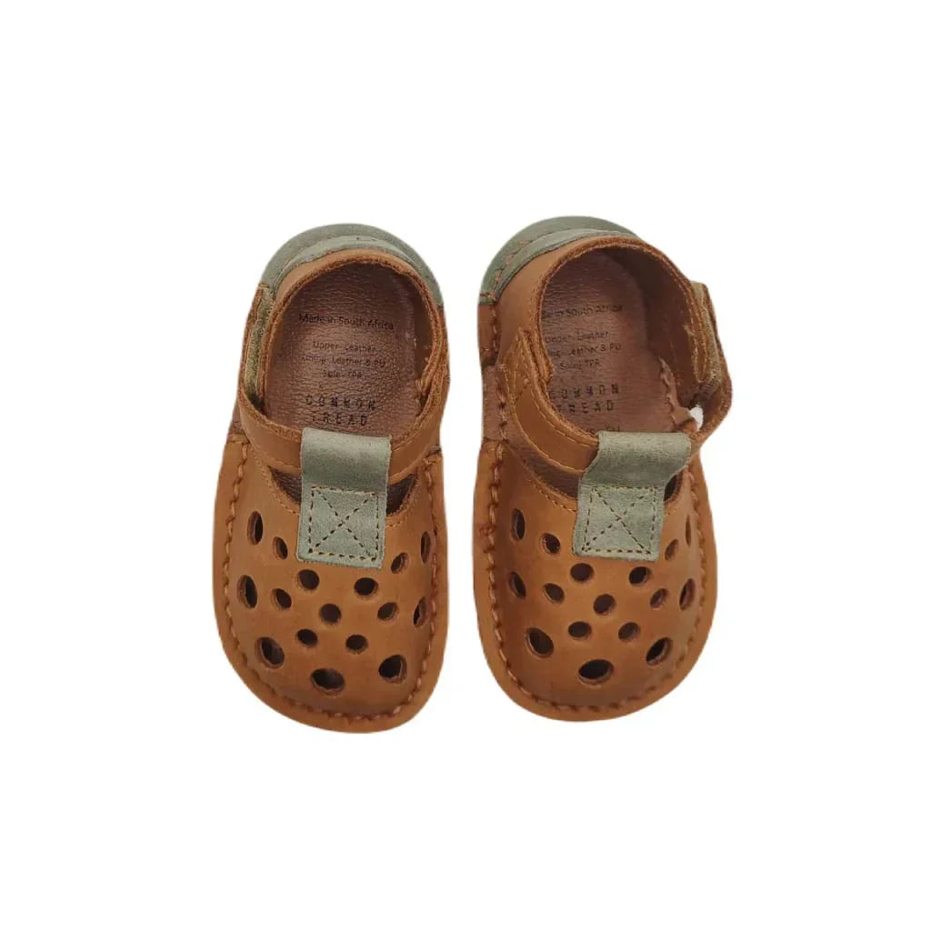 Pair of brown leather baby shoes with ventilation holes and green accents on white background
