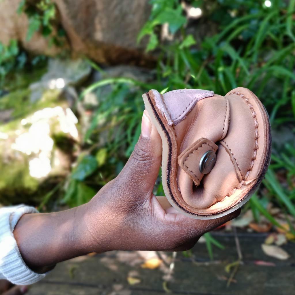 Hand holding a compact, foldable tan leather wallet outdoors with green plants in the background