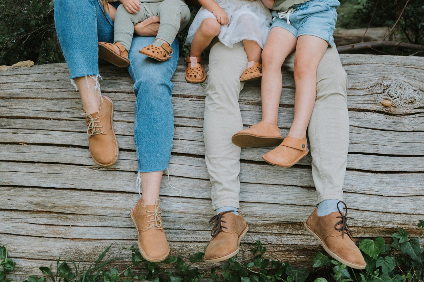 Two adults and two children sitting on a wooden log with their feet dangling.