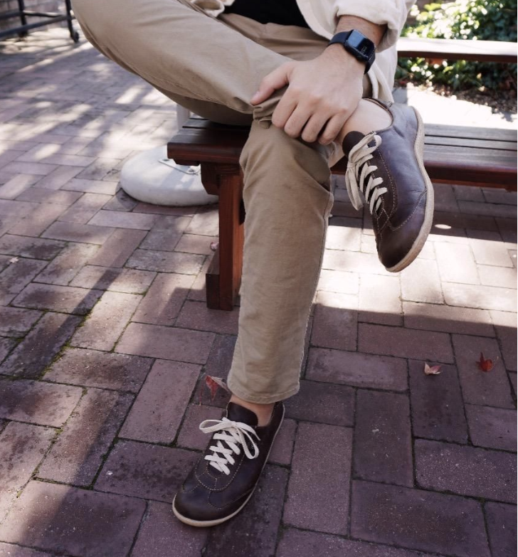 Person sitting on a bench wearing beige pants and black sneakers with white soles.