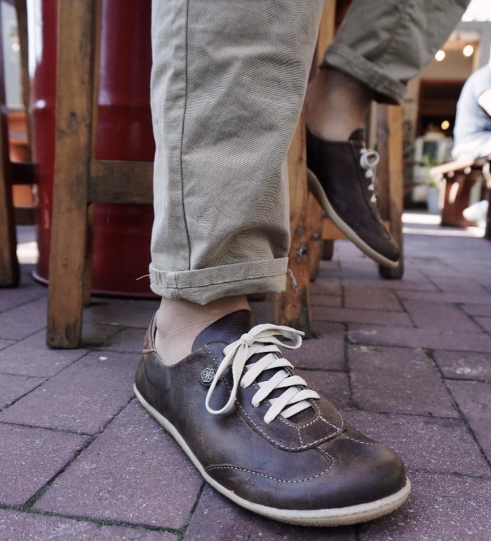 Brown leather shoes with white laces worn on a paved outdoor floor.