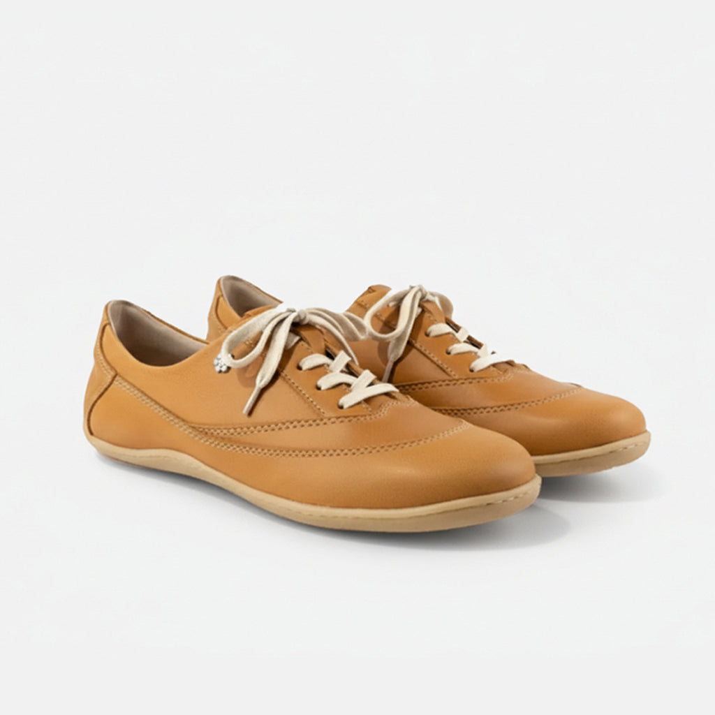 Pair of tan leather shoes with white laces on a light gray background