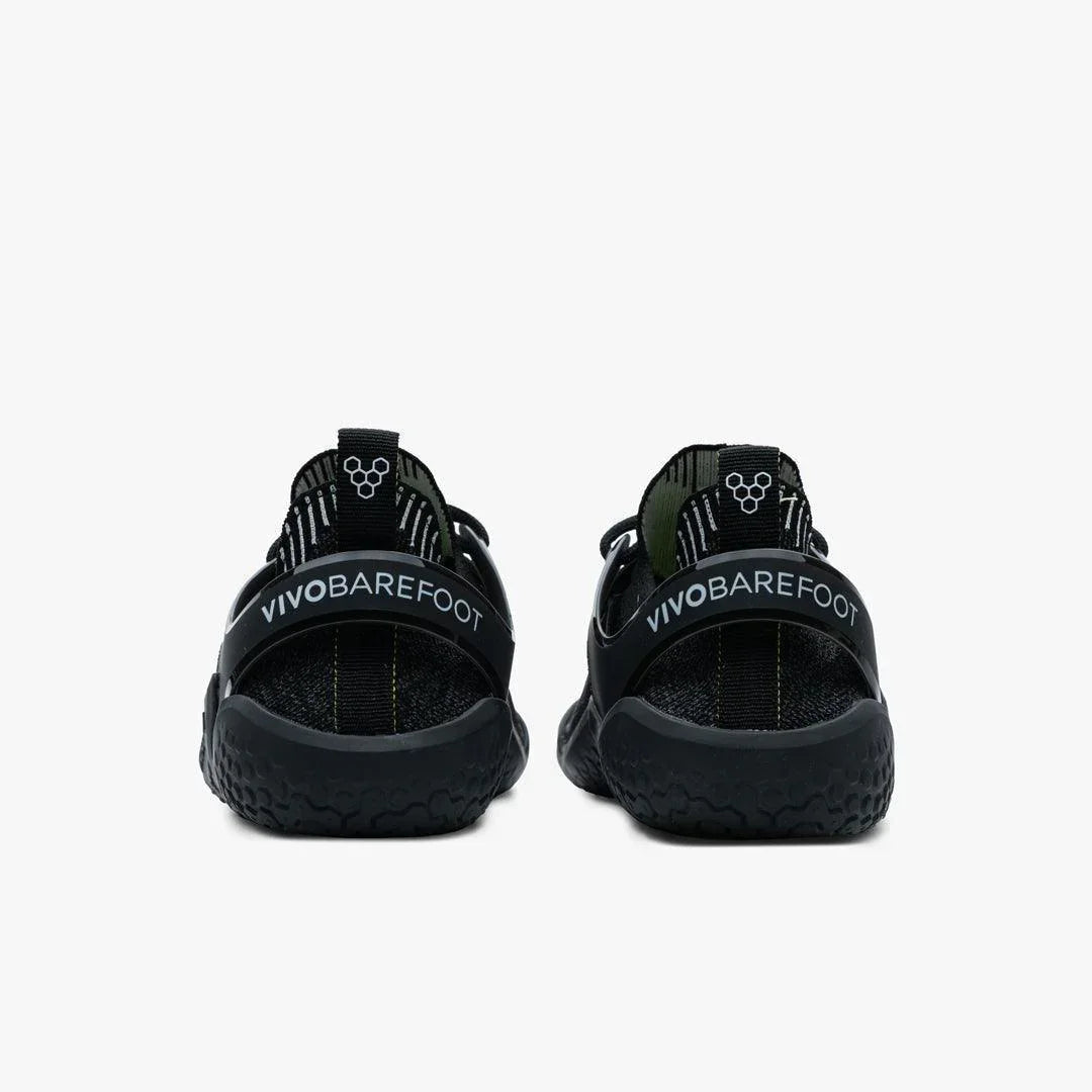 Rear view of black Vivobarefoot Motus Strength men's shoes with textured soles on white background